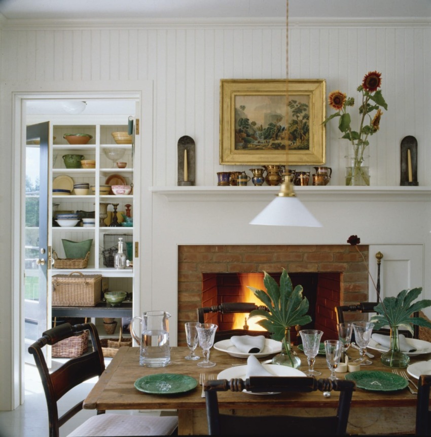 Cozy dining room with a brick fireplace, table set for dinner, and open shelves displaying colorful dishes in the background.