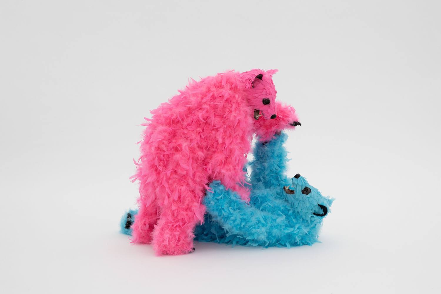 Two colorful furry bear sculptures playing, one pink and one blue, on a plain white background.