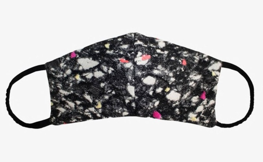 Black and white face mask with colorful speckles and adjustable ear loops placed on a light background.