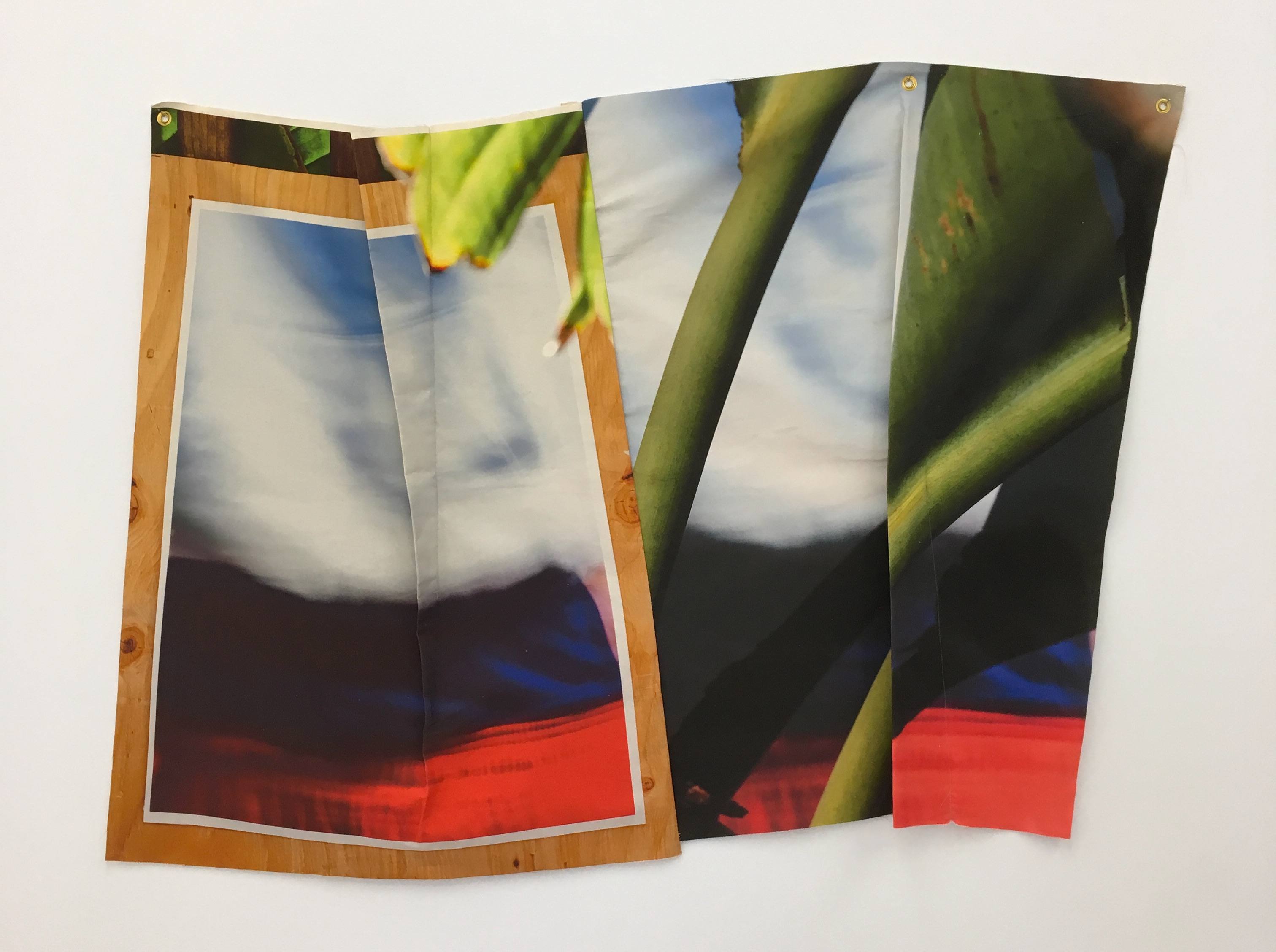 Abstract artwork with blurred colors in blue, red, and green on overlapping fabric pieces, mounted against a white wall.