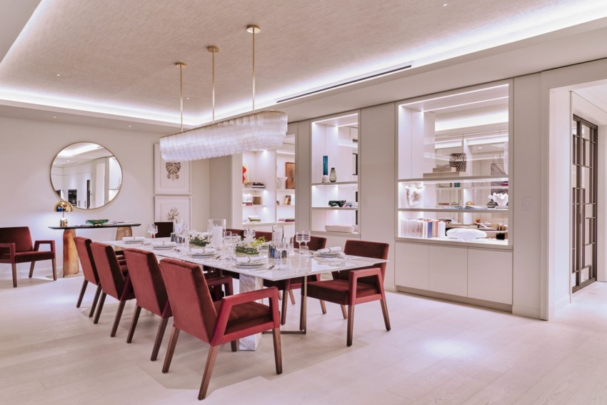 Elegant dining room with a large table, red chairs, modern chandelier, and decorative shelves.