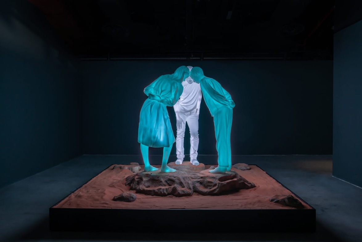 Three glowing figures bending over rocky terrain in dimly lit room.