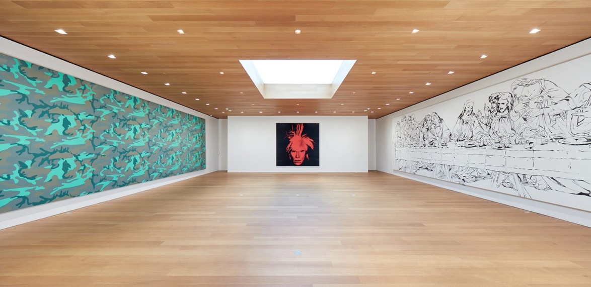 Art gallery with wooden floors, featuring modern artworks on walls, including a colorful abstract piece and monochrome designs.