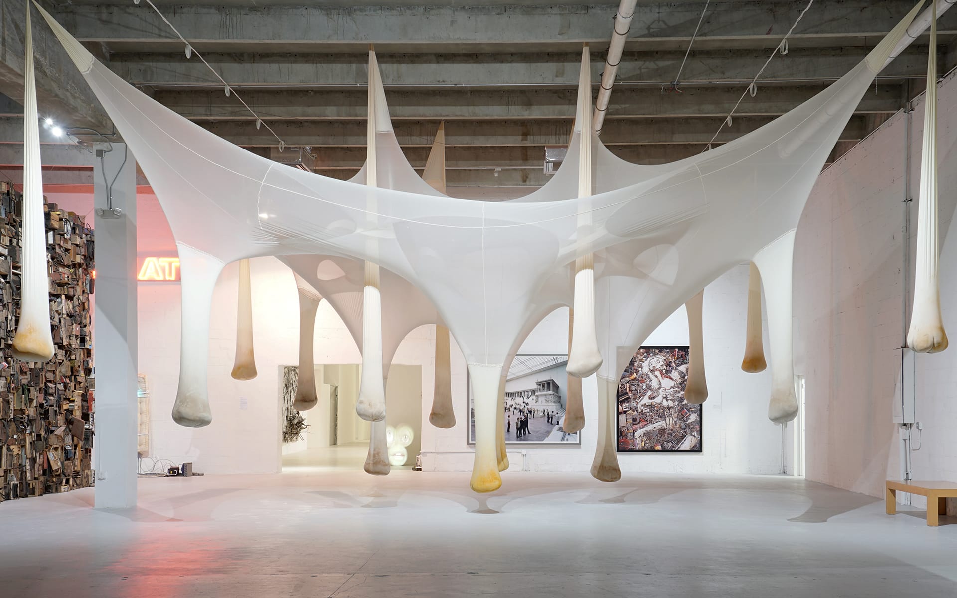 Modern art installation featuring large white fabric structure suspended from ceiling in a spacious gallery setting.