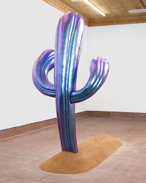 Metallic purple cactus sculpture displayed in a modern gallery space with a wooden ceiling and tiled floor.