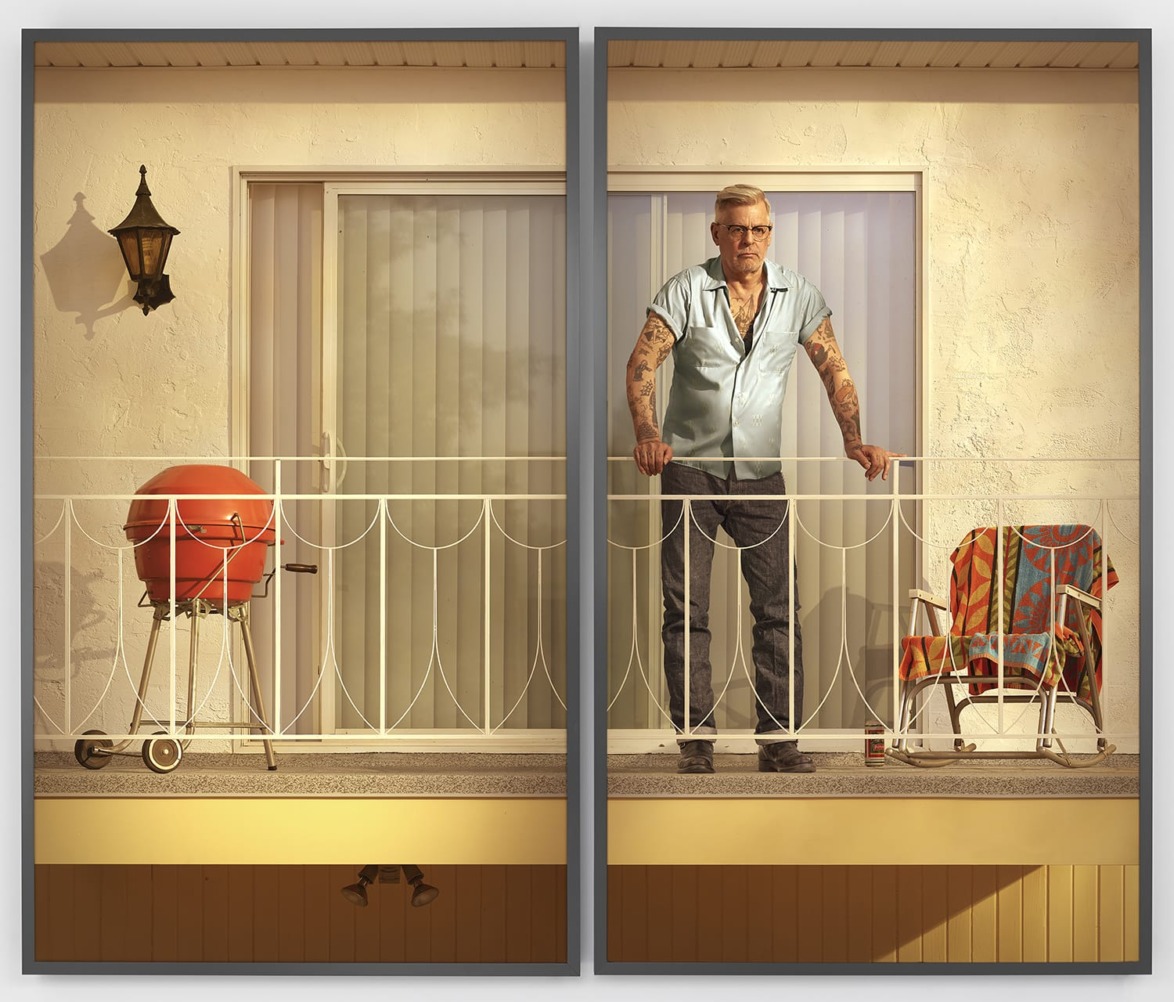 Person standing on a balcony next to a barbecue grill and a colorful chair, with a light fixture on the wall.