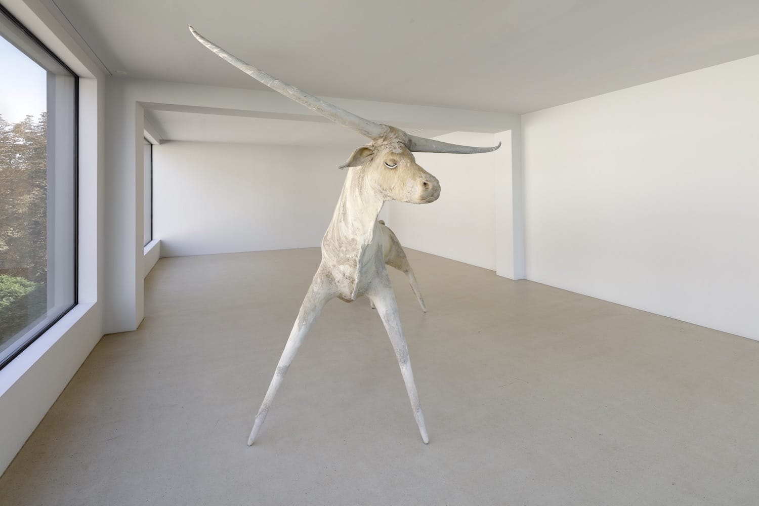 Sculpture of a white unicorn with elongated limbs and horn in a minimalistic gallery space.