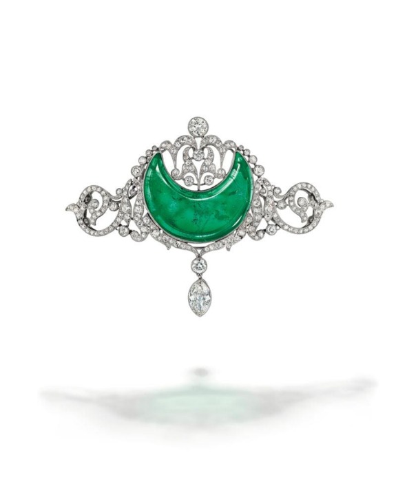 Ornate jewelry brooch with a green crescent stone, intricate silver detailing, and sparkling diamonds on a white background.