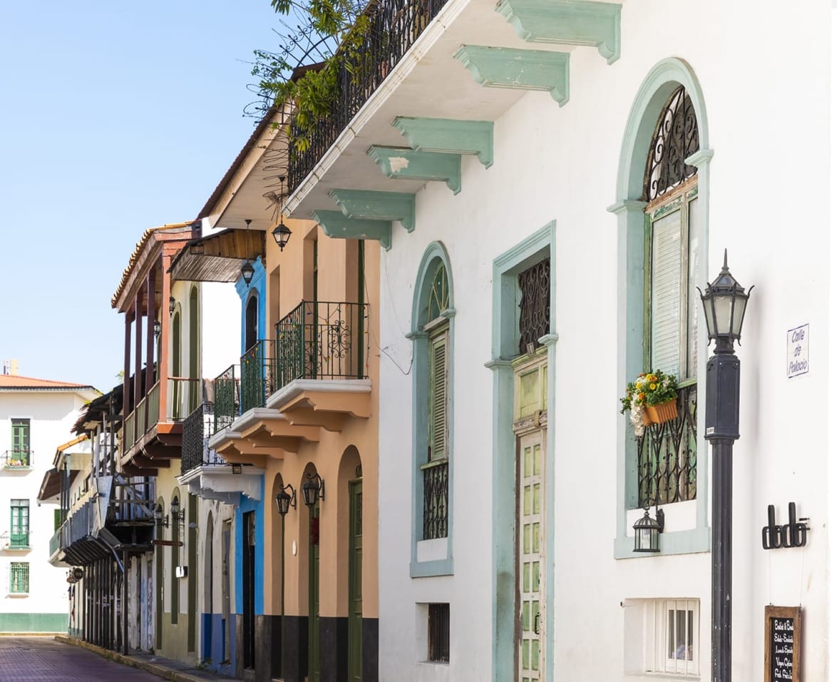 Colorful historic buildings with balconies on a street lined with lampposts in a sunny urban setting.