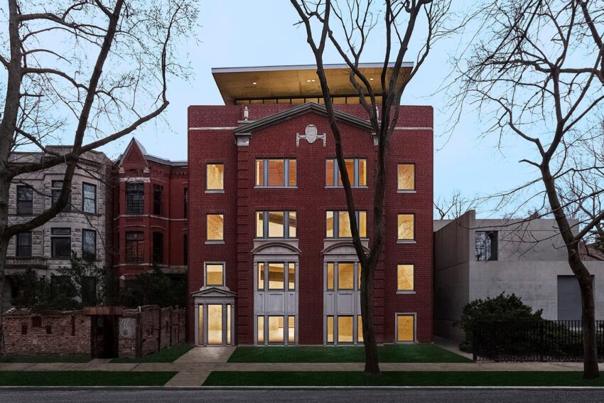 Red brick building with large windows and surrounding trees at dusk.
