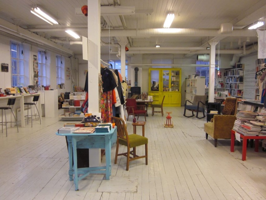 spacious bookstore with wooden floors, diverse furniture, shelves filled with books, and bright natural light from large windows
