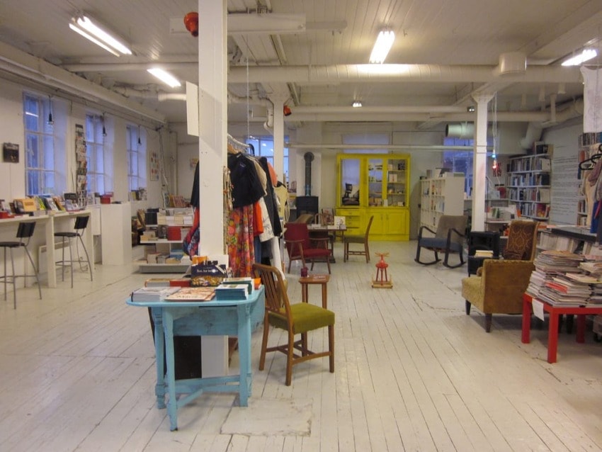 spacious bookstore with wooden floors, diverse furniture, shelves filled with books, and bright natural light from large windows
