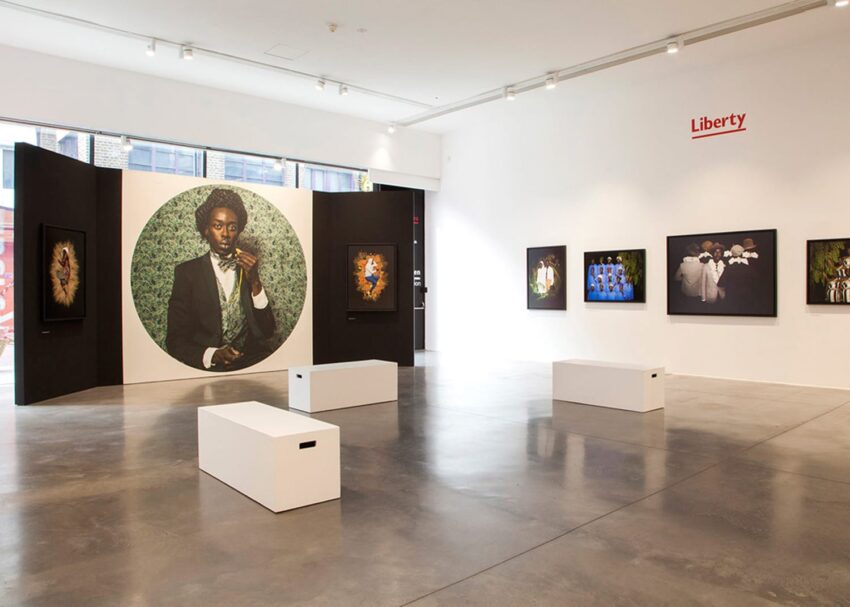 Art gallery interior with large portrait and framed artworks on walls; white benches in the center of a spacious room.