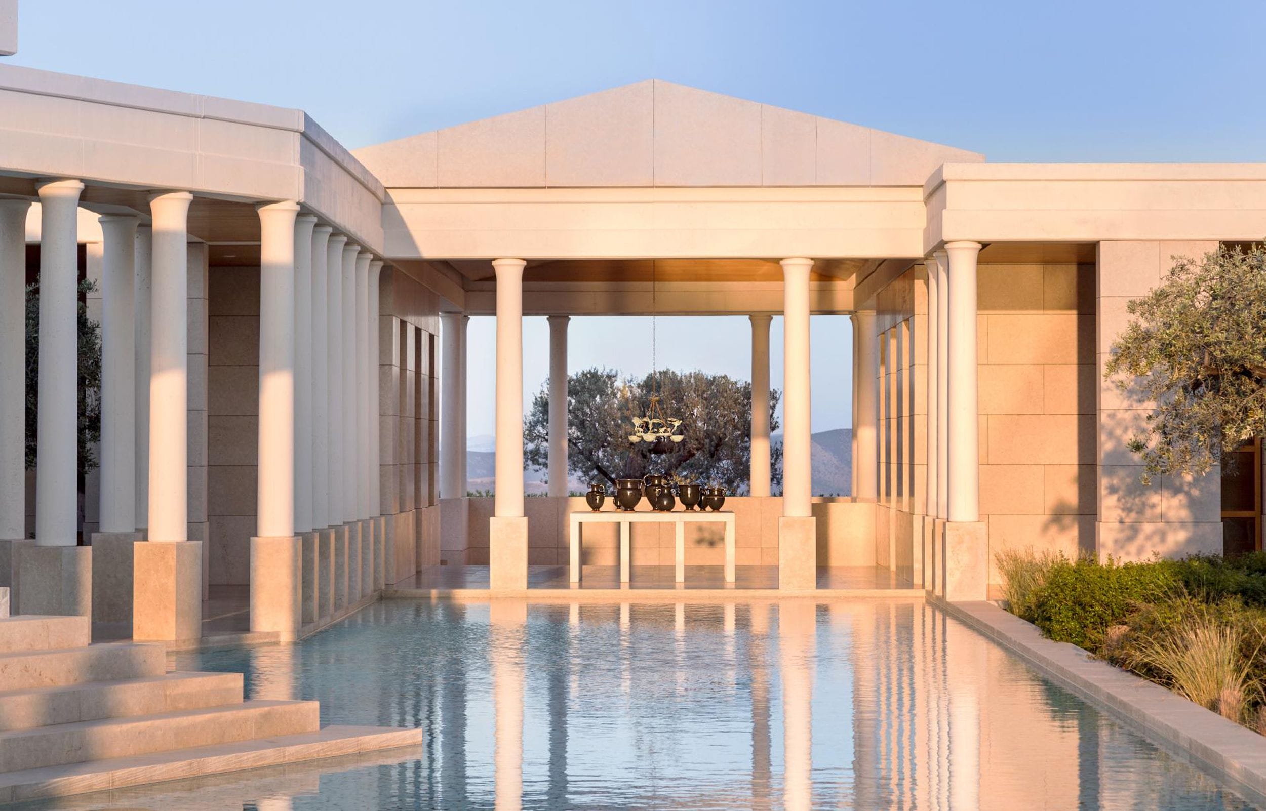 Elegant building with tall columns and a tranquil reflecting pool in the foreground at sunset.
