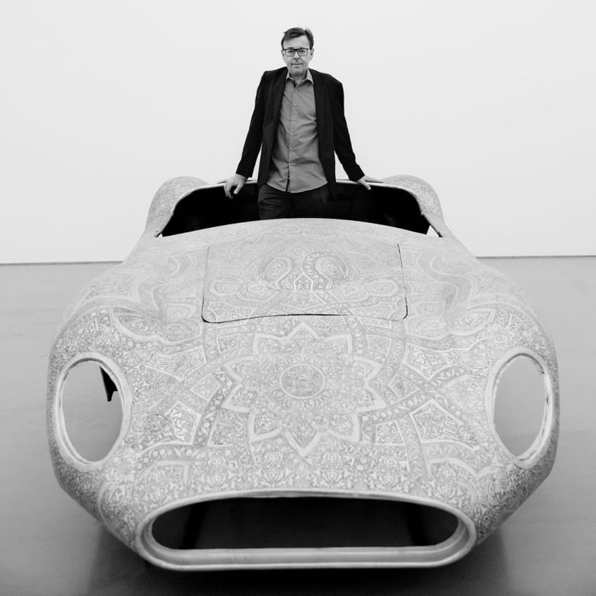 Man standing behind a detailed, patterned vintage car model in a monochrome setting
