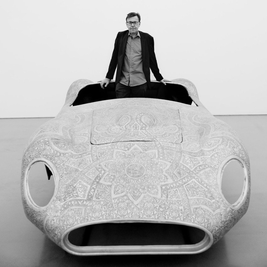 Man standing behind a detailed, patterned vintage car model in a monochrome setting