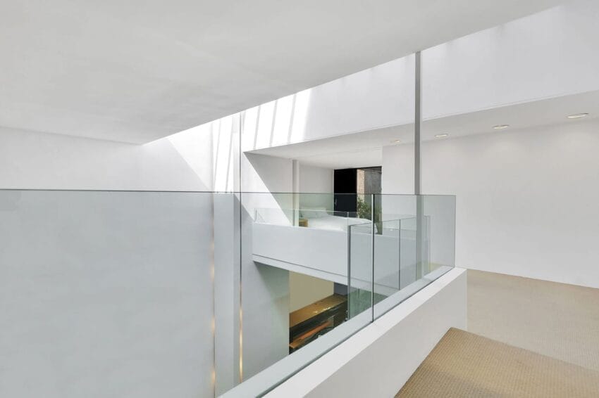 Minimalist interior with white walls, glass railings, and natural light streaming through a large window, creating a modern look.