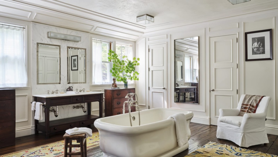 Spacious bathroom with freestanding tub, large mirrors, elegant white decor, and wooden flooring.
