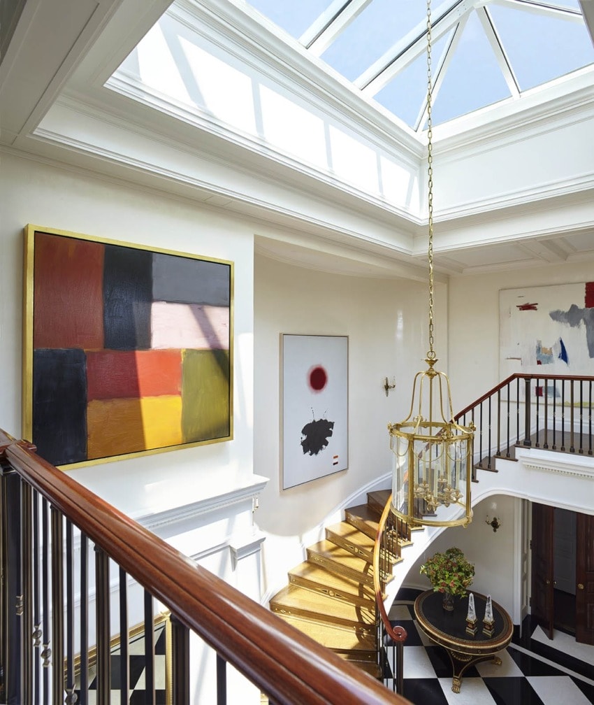 Elegant two-story foyer with modern art, skylight, chandelier, wooden staircase, and checkered black and white floor.
