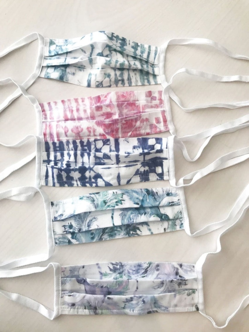 Five colorful tie-dye face masks with white straps laid out on a white surface.