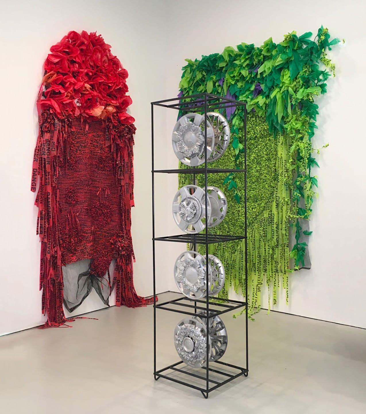 Colorful textile art installations with red and green fabric designs on walls, metal framework with circular elements in foreground.