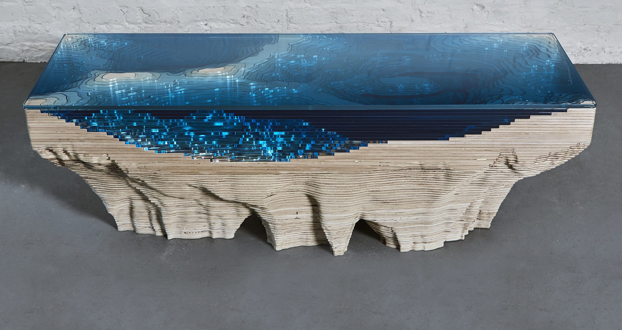 Modern artistic table resembling a topographic landscape with blue resin and layered wooden design.