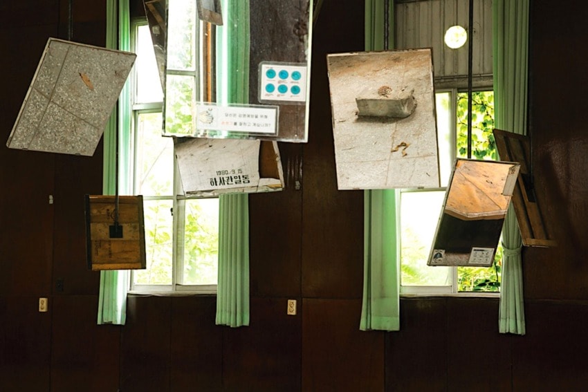Art installation with floating mirrors and boxes in a room with wooden walls and green curtains.