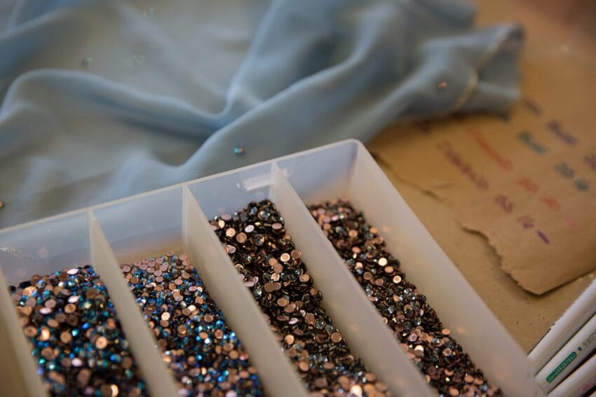 Box of colorful rhinestones with a blue fabric in the background.
