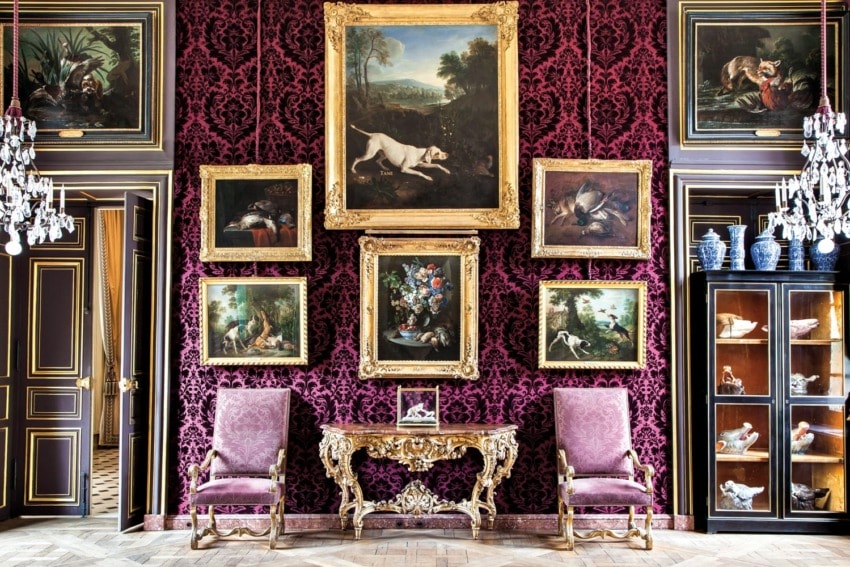 Luxurious room with ornate paintings, a decorative table, and purple patterned walls, exuding an elegant and classical ambiance.