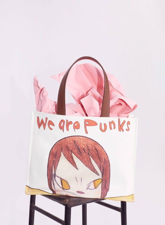 Tote bag with "We are Punks" design, featuring a cartoon face, sitting on a stool with pink tissue paper inside.