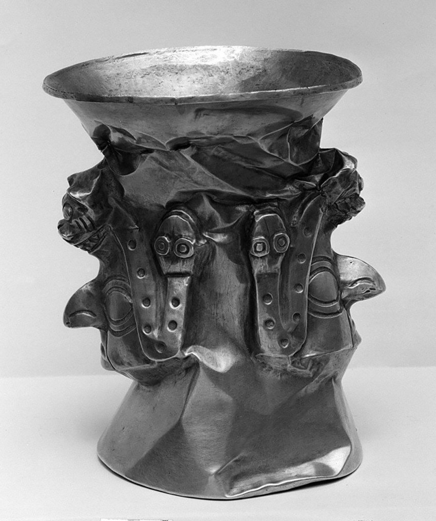 Ancient metal ceremonial vessel with intricate carvings and faces, showcasing detailed artistic craftsmanship.