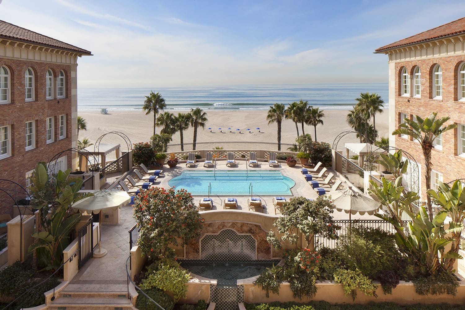 Beachfront hotel pool with lounge chairs, surrounded by palm trees, and ocean view in the background.