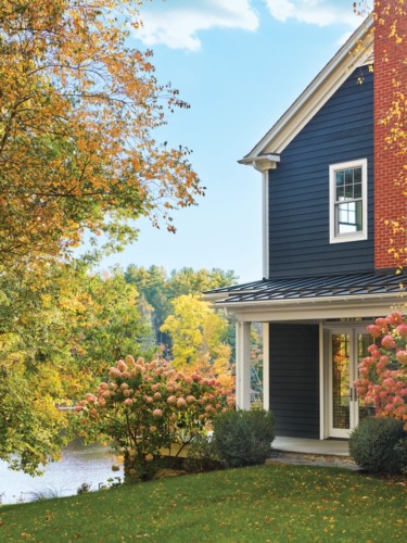 Blue house with autumn foliage, hydrangeas, and a view of a lake. The sun casts a warm glow on the landscape.