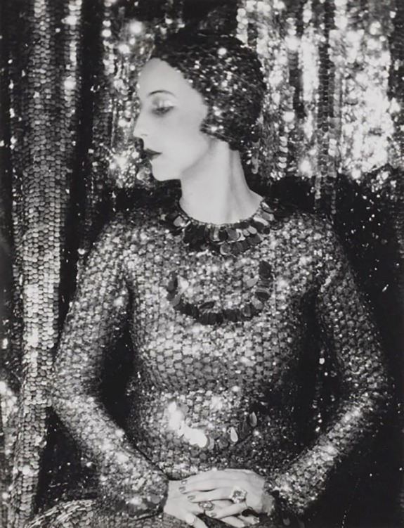 Woman in a vintage sequined dress and headpiece, posing elegantly against a backdrop of shimmering sequins.