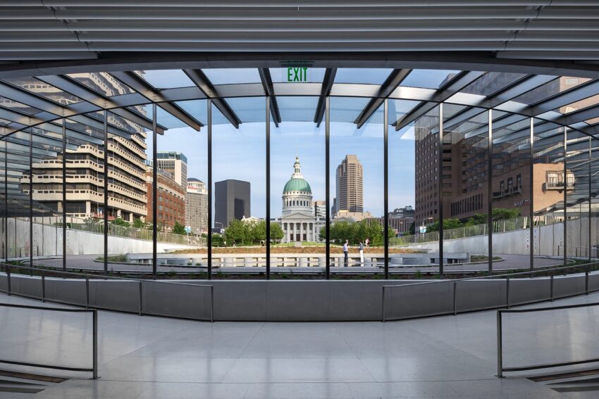 View of historic building and skyline through large modern glass windows with exit sign, captured in a panoramic perspective.