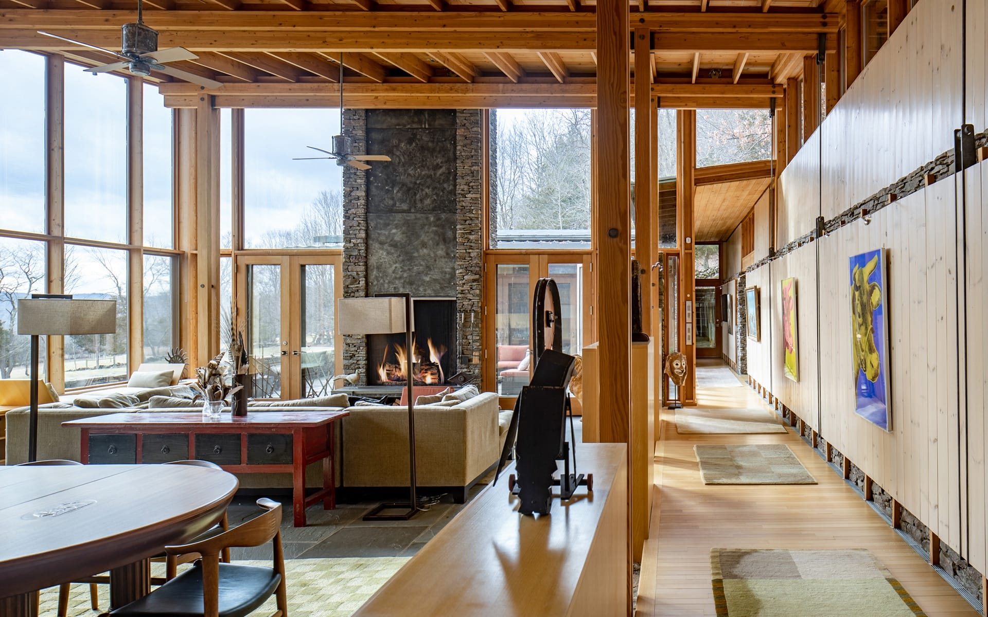 Spacious modern living room with large windows, a fireplace, and contemporary artwork on wooden walls.