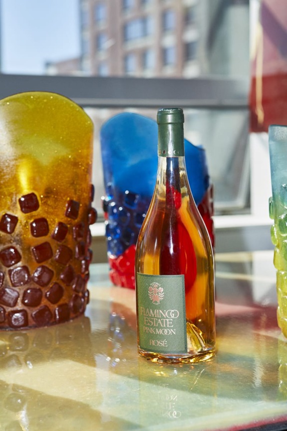 Bottle of Flamingo Estate Pink Moon Rosé on a colorful surface with artistic glass sculptures in the background.