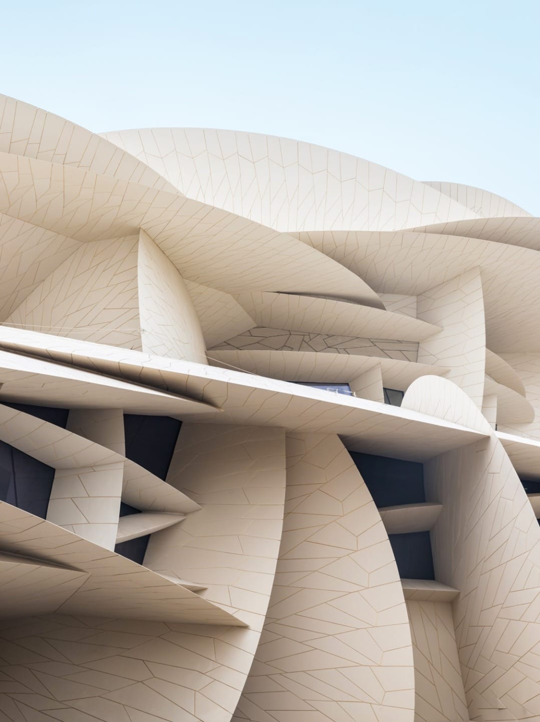 Modern architectural design with overlapping beige panels and windows, creating an abstract and dynamic facade against blue sky.