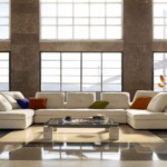 Modern living room with white sectional sofa, colorful cushions, coffee table, and large windows with natural light.