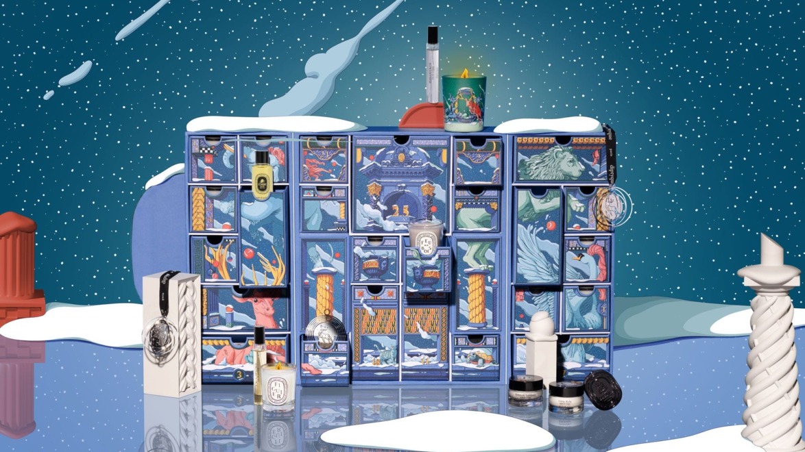 Advent calendar with colorful illustrations, luxury skincare and fragrance products on a snowy reflective surface.