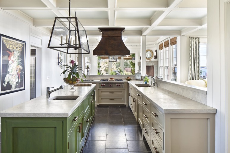 Spacious kitchen with green island, white cabinets, large windows, and a vintage poster on the wall.