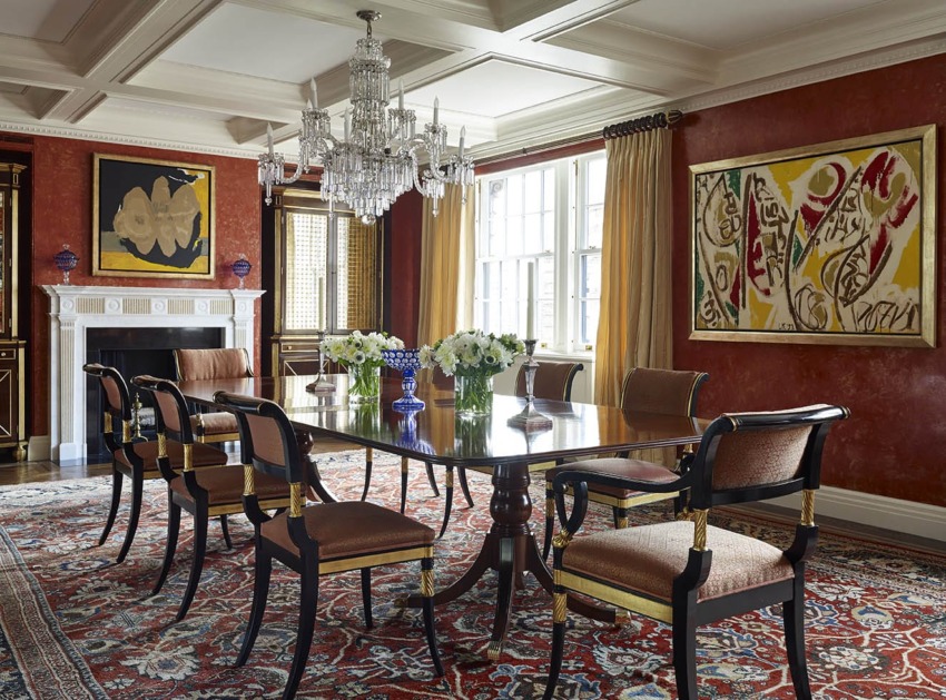 Elegant dining room with large table, upholstered chairs, ornate chandelier, vibrant red walls, and abstract artwork.
