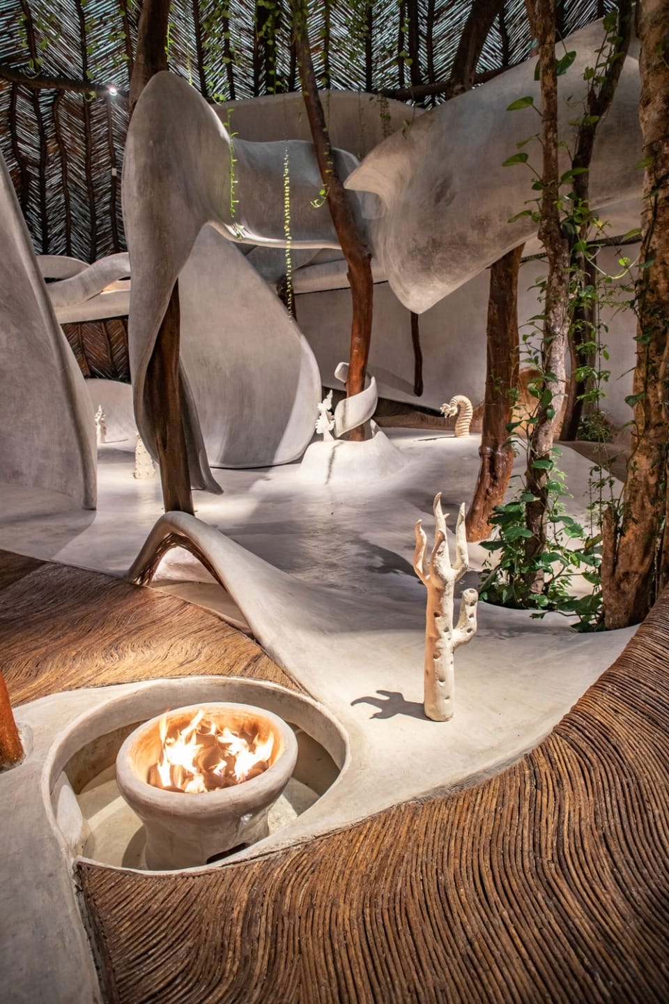 Nature-inspired interior with organic shapes, trees, a fire pit, and sculptural elements creating a harmonious natural atmosphere.