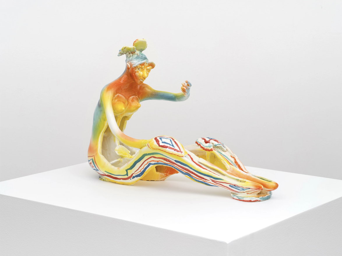 Colorful abstract sculpture of a seated, elongated human form with intricate patterns, displayed on a white pedestal.