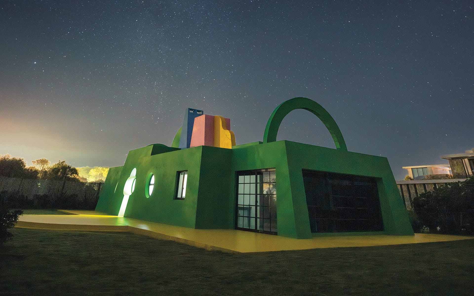 Modern green house with colorful roof under a starry night sky.