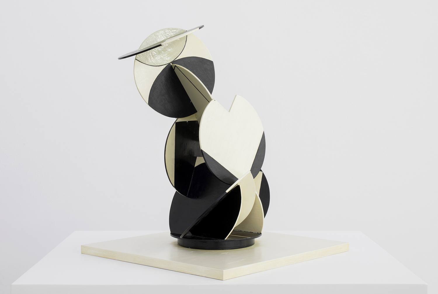 Abstract black and white geometric sculpture with circular and angular shapes on a square base.