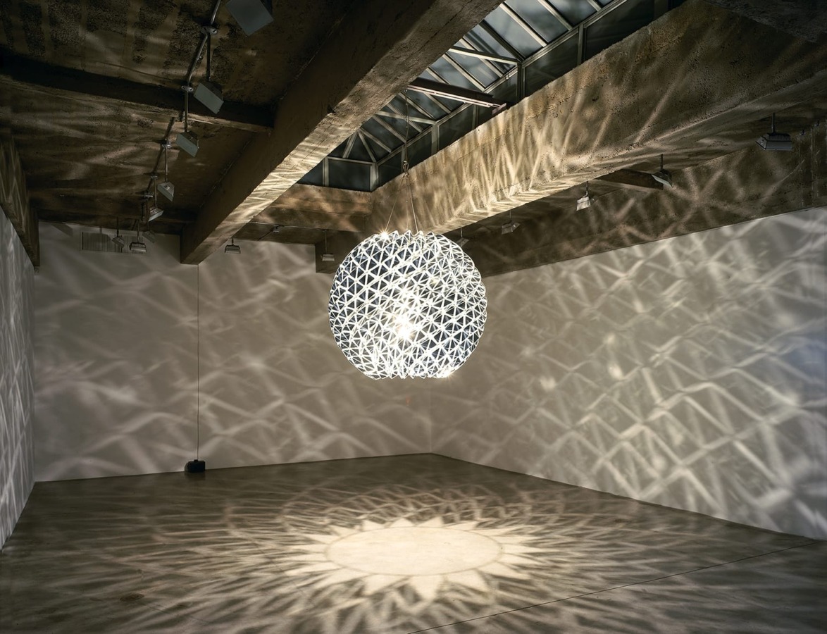 Large spherical light fixture casting intricate shadow patterns in a dimly lit, modern industrial-style room.