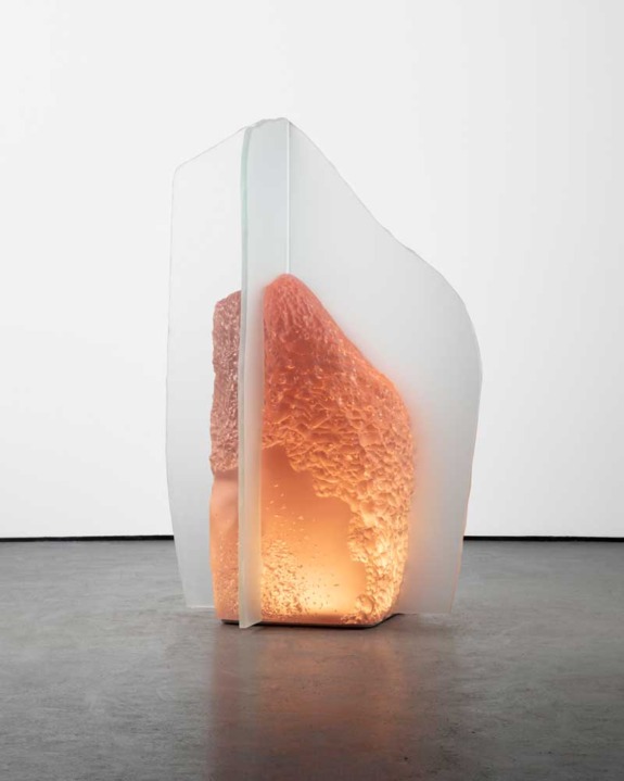 Large abstract sculpture with glowing orange interior and translucent outer layer on display in a gallery setting.