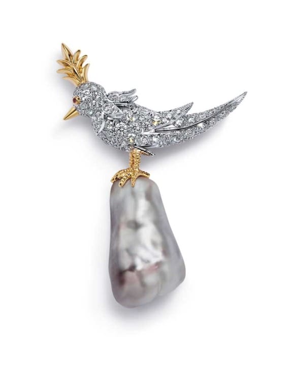 Diamond-encrusted bird brooch with golden crest perched on a large pearl, elegant and intricate jewelry design.