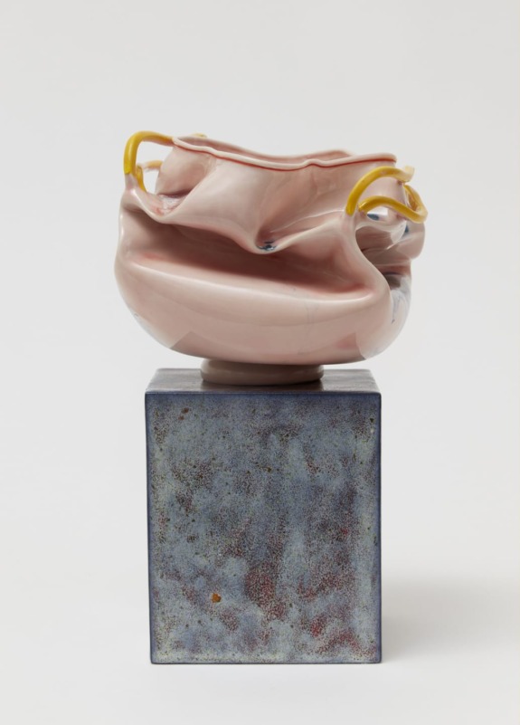 Sculptural ceramic artwork with a pink, twisted form and yellow handles displayed on a textured square base.